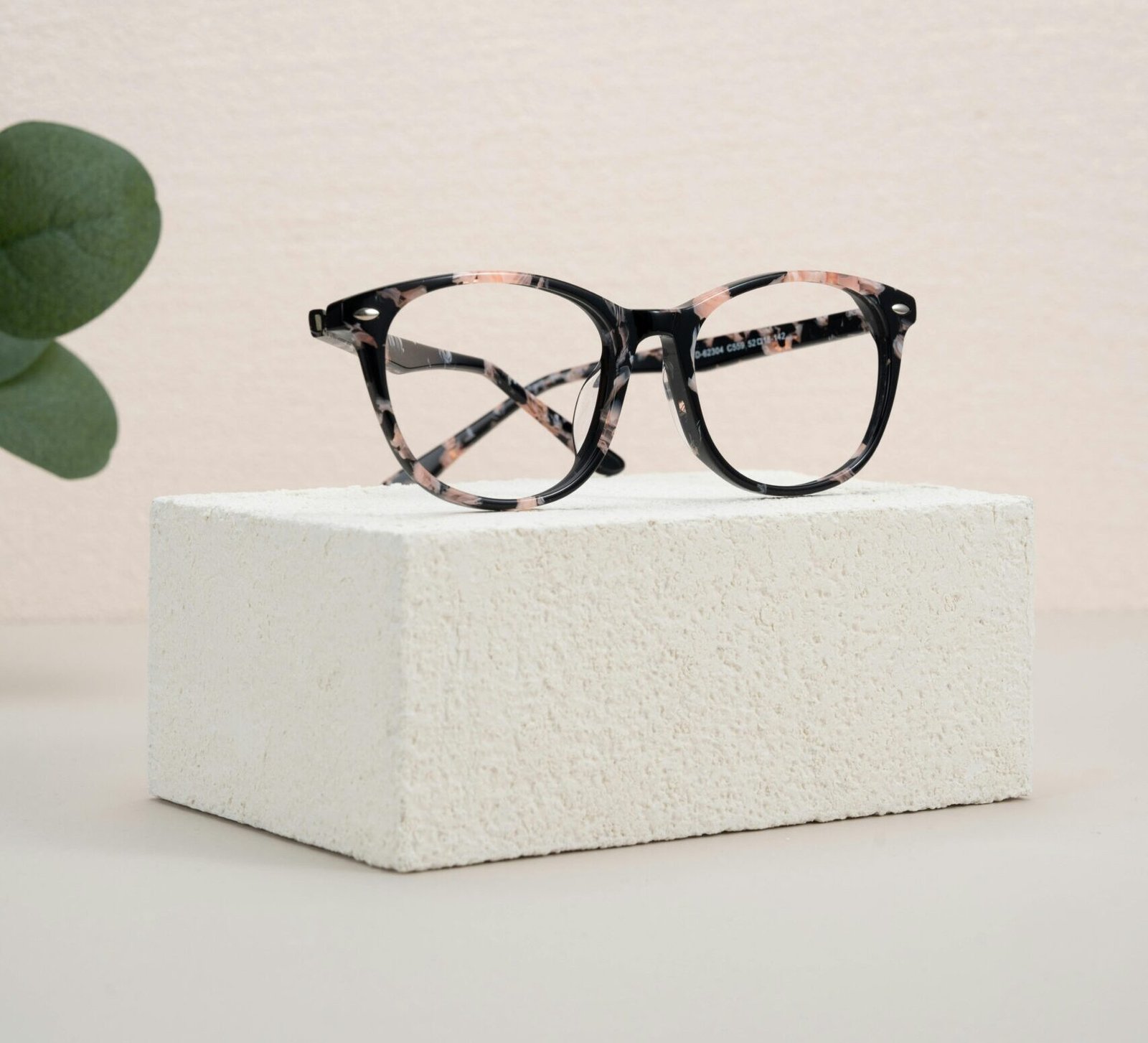 Elegant eyeglasses resting on a white textured block with minimalist design elements.