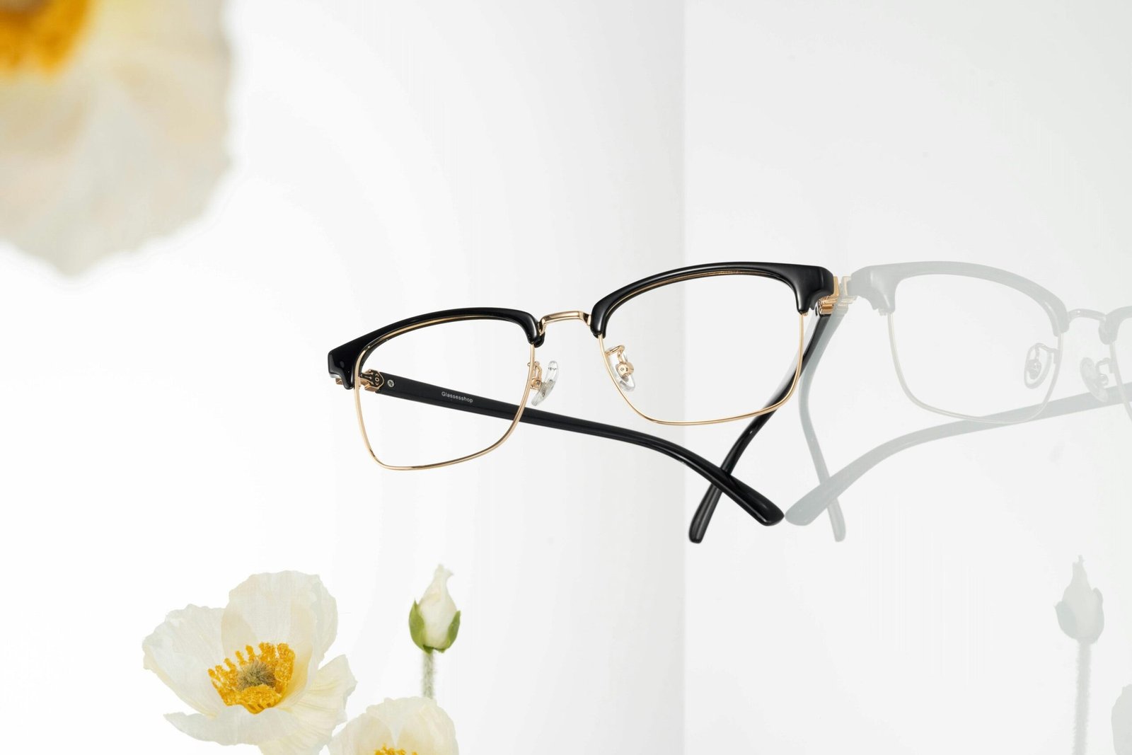 Stylish black and gold eyeglasses with white flowers on a reflective surface.